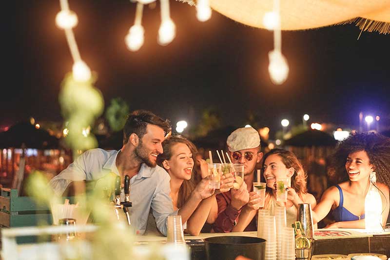 Happy friends cheering and drinking cocktails at beach party outdoor