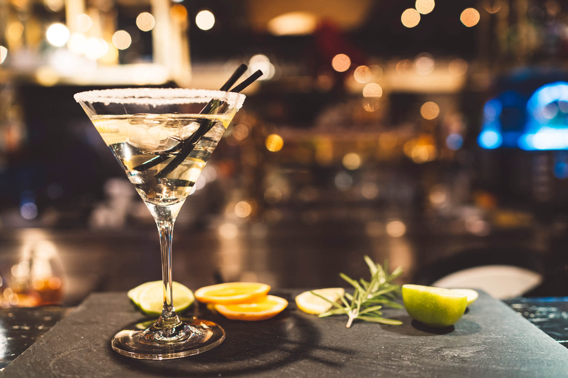 Glass of martini with lemon and rosemary on bar