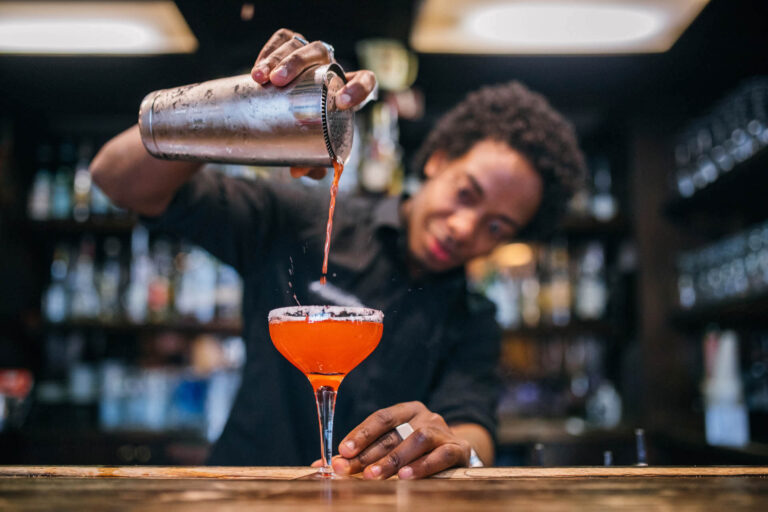 Man pouring cocktail from cocktail shaker in bar